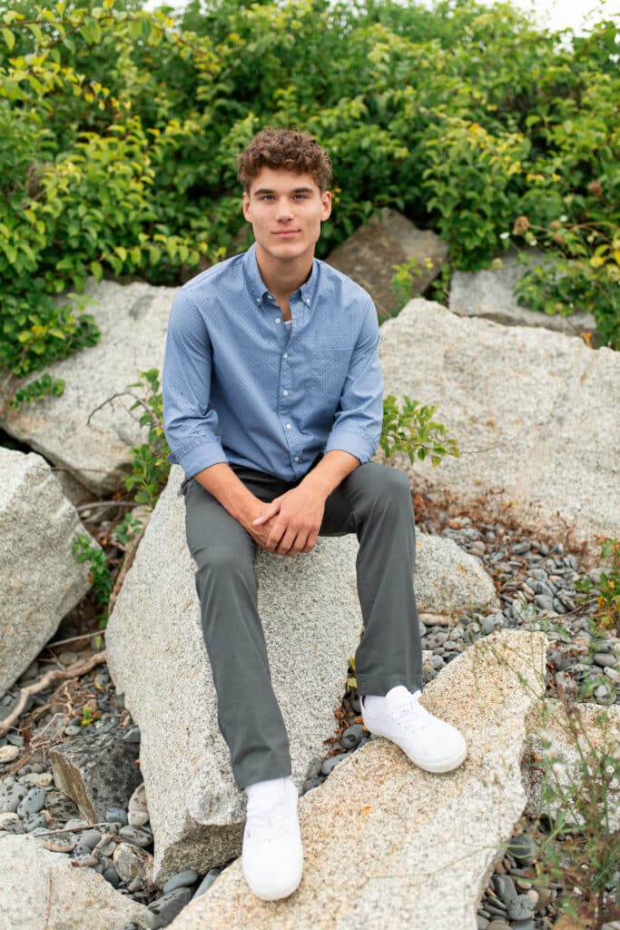 teen boy sitting on a rock with his feet resting on an angled rock, one knee higher than the other