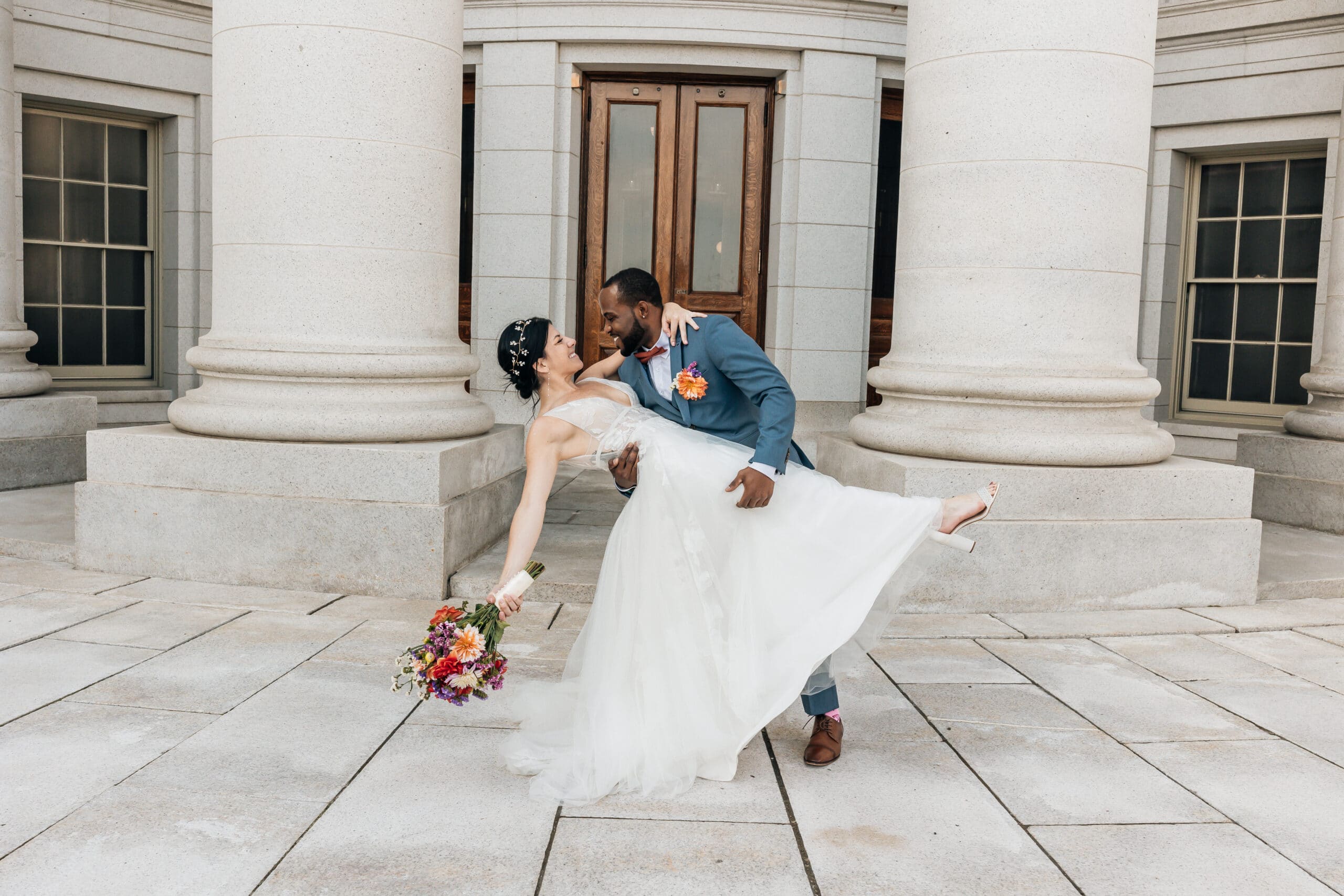 Wedding portrait of couple Jaime & Cedric outside a stone building with large pillars.