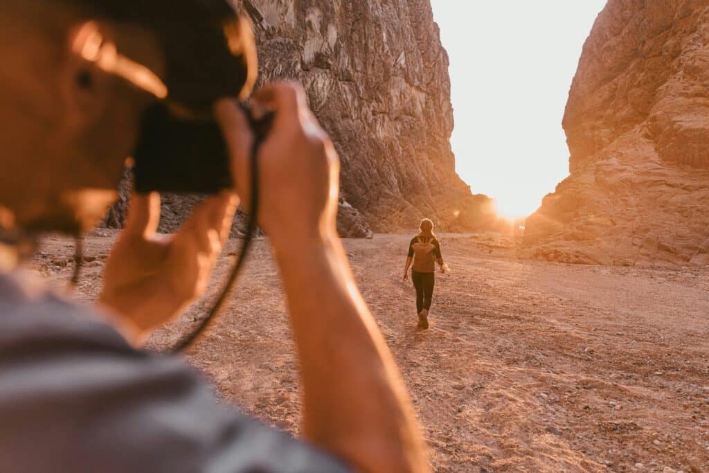 photographer taking pictures of woman walking toward sunset in a canyon in Saudi Arabia.