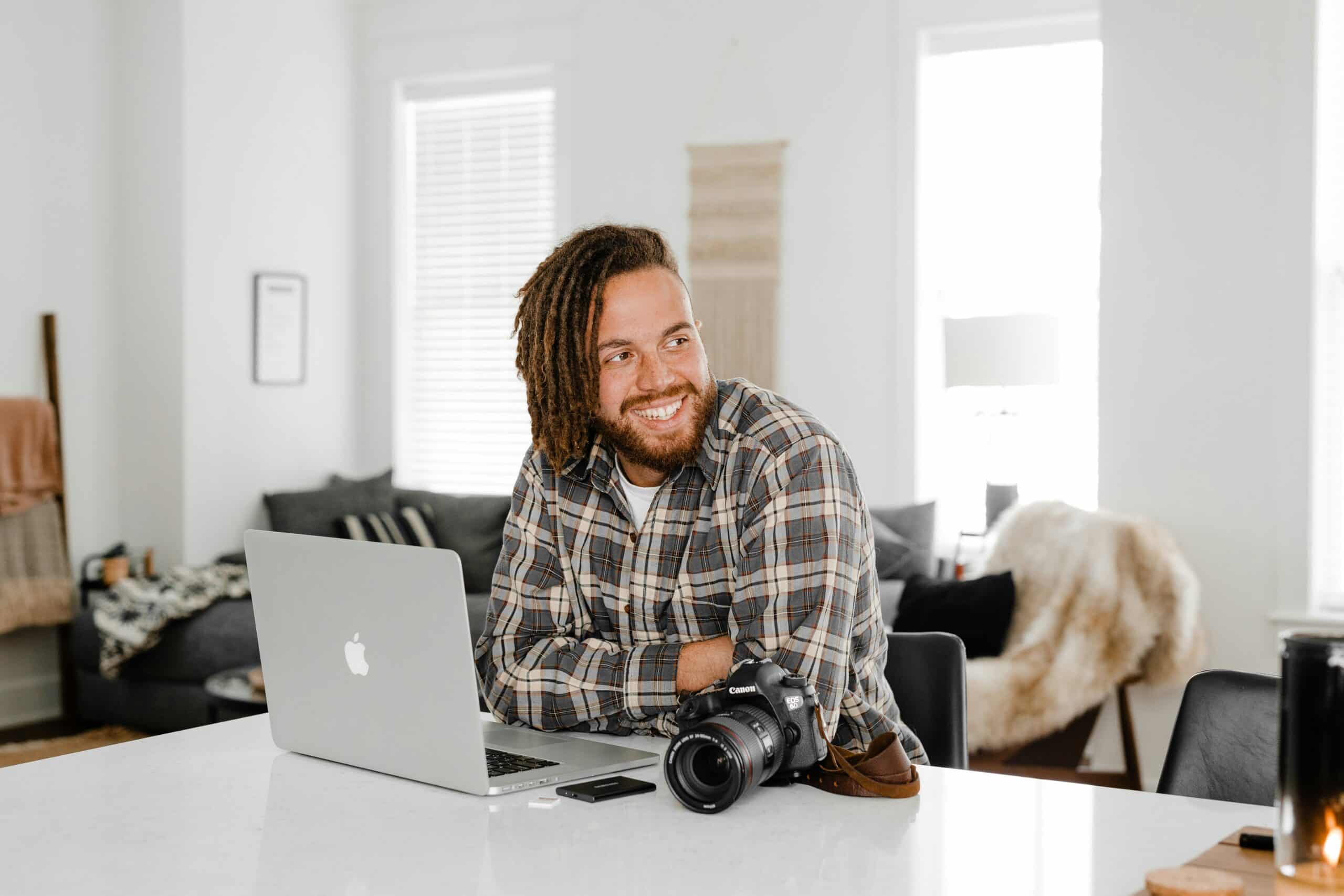 man in black and white plaid dress shirt sitting beside macbook