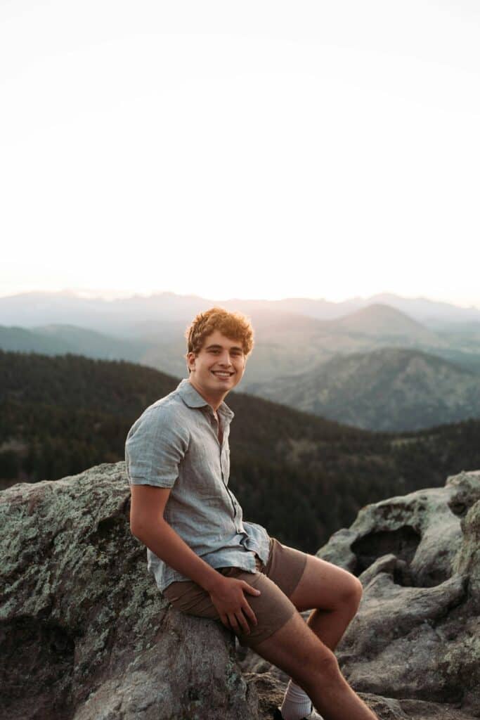 senior boy sitting on rock with mountains in background